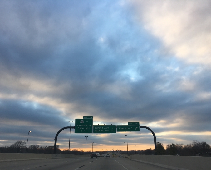 [Clouds with a sunset on the horizon, offset by a highway exit sign]